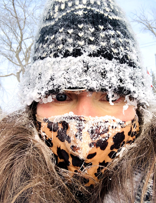 photo: outdoor portrait of a student wearing a frost-covered toque, frost-covered 'lepard-design' face covering, and frost in her hair